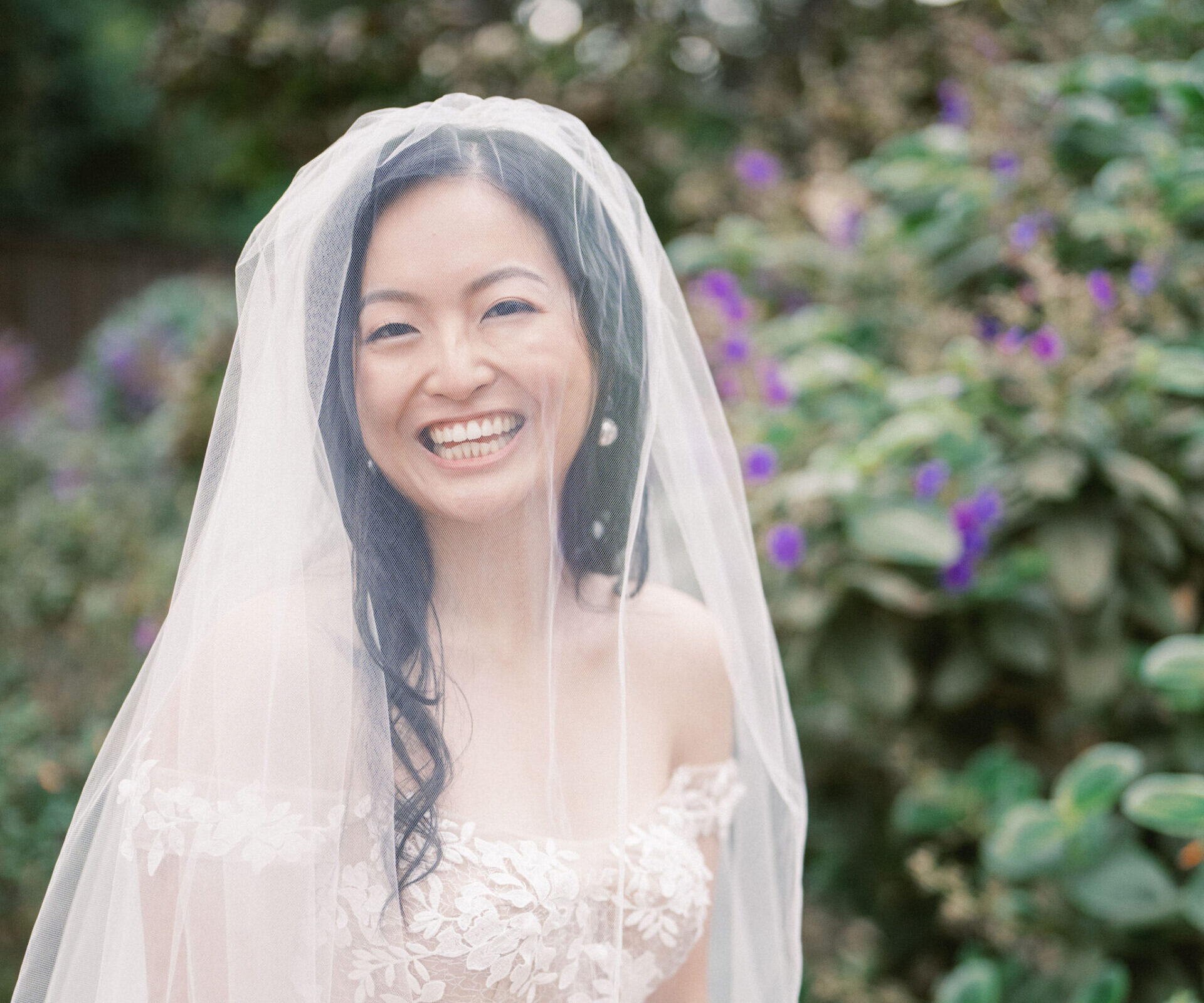 Bride Jie's flawless Kohnur elegant bridal updo and veil, featuring radiant timeless wedding makeup, posing with groom Everrete in a formal Montecito archway.
