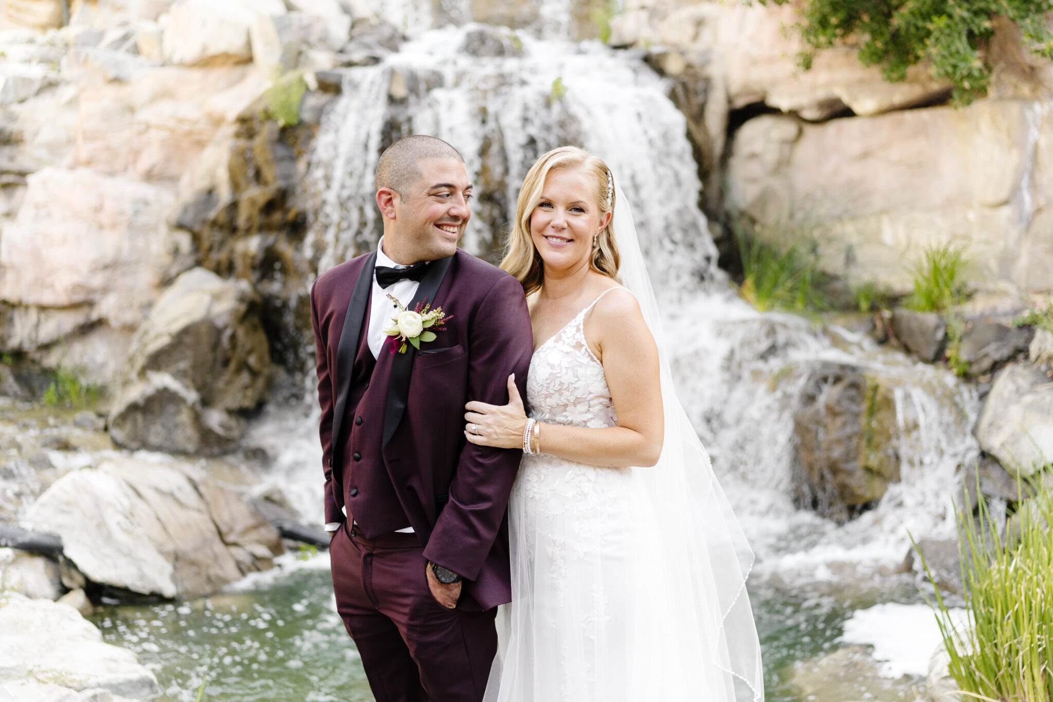Close-up of Bride Kristin with a stunning side-swept Kohnur romantic wedding hairstyle secured by a crystal clip, and luminous soft glam bridal beauty makeup, embracing groom Gino at The Marquess.