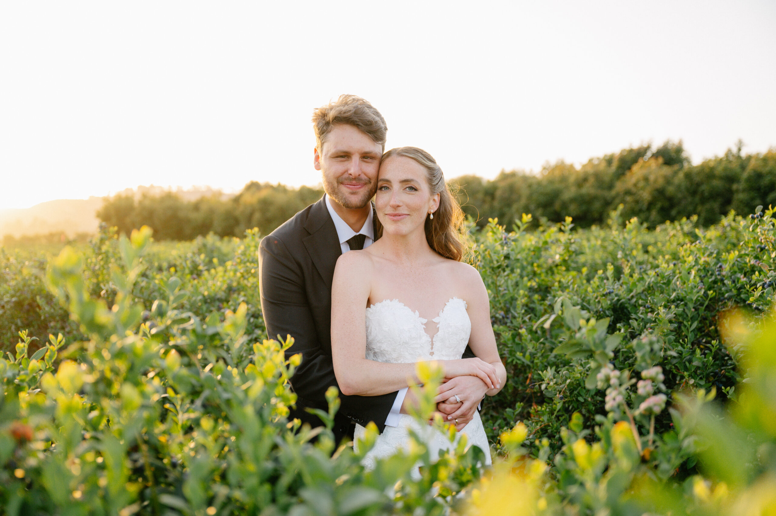 Bride Adar with long, flowing, Kohnur romantic wedding hairstyle and natural, luminous timeless wedding makeup, posing with groom Oliver in a lush, green garden.