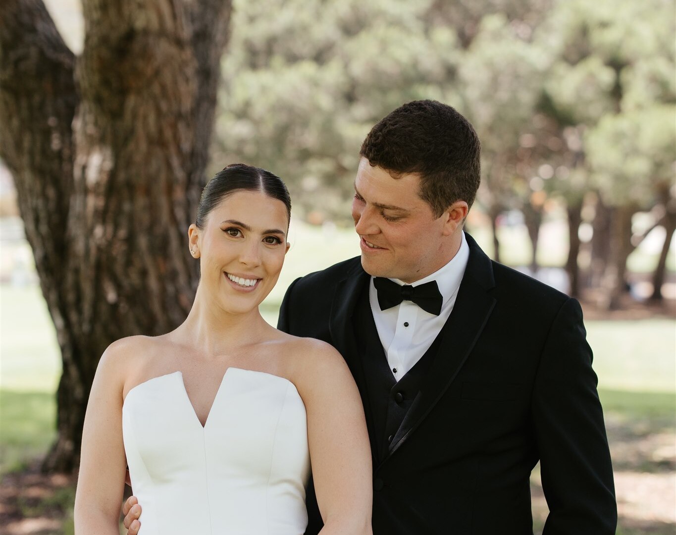 Bride Katie with a chic, polished Kohnur elegant bridal updo and radiant soft glam bridal beauty makeup, posing with groom Matt on the lush lawn at The Ranch Laguna Beach.